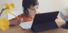 boy with headphones sitting at desk looking closely at a laptop/tablet screen