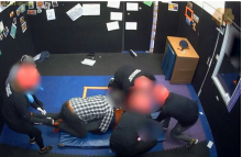 multiple adults pressing a child to the ground in prone position