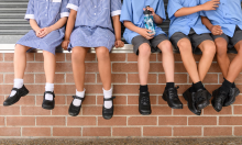 legs of 5 school students who are sitting on a brick wall