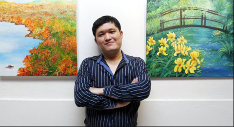Dennis Liew between two of his paintings hung on a wall