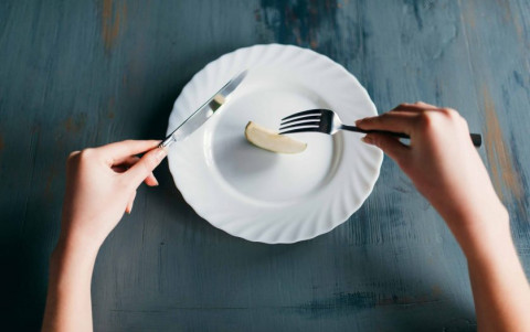 hands with knife & fork on a near-empty plat