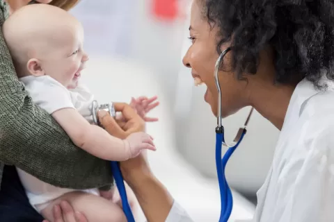 health worker with stethoscope testing a smiling baby (in parent's arms)