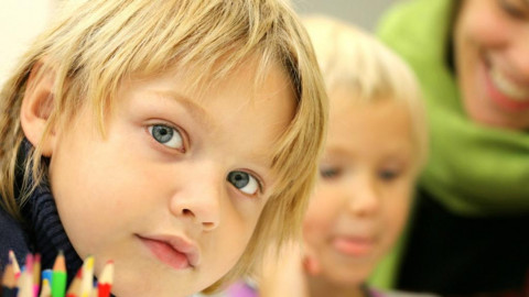 young child looking towards camera - out-of-focus second child & adult