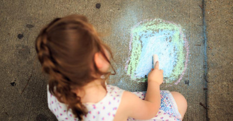 view if girl drawing with chalk on a footpath