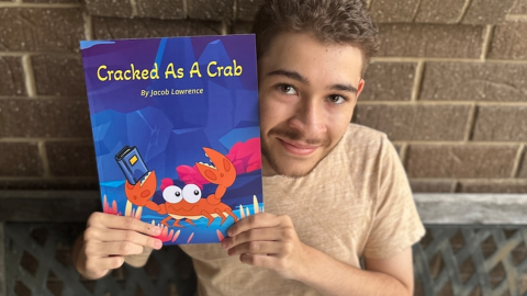 jacob smiles ay camera, holding up a copy of his book