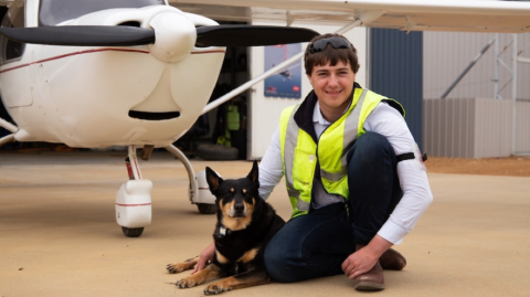 young man and dog squatting in front of a light aircraft