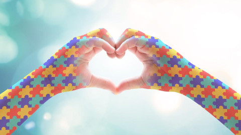 hands make a heart (love) shape, on forearms with coloured puzzle pieces