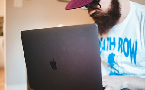 man with beard, glasses and cap using a laptop computer