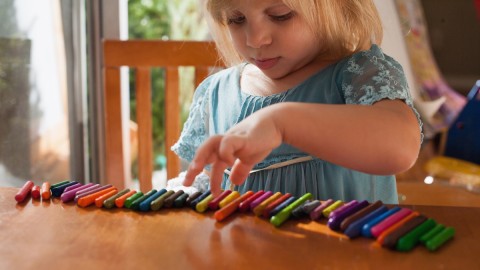 girl playing with lined-up crayons