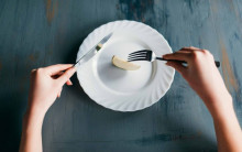 hands with knife & fork on a near-empty plat