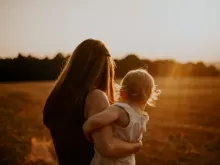 mother with child on hip facing away from camera into sunset