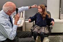 doctor inspecting the eye of a young girl sitting in a chair facing him