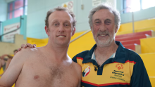 Peter Thorn and his father John standing side-by-side and smiling. Peter looks like he's ready to go swimming. John's top says "Special Olympics Australia, Greater Canberra". 