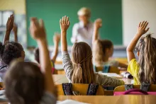 students in a mainstreream classroom (with their hands raised) - teacher with blackboard at from