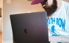 man with beard, glasses and cap using a laptop computer